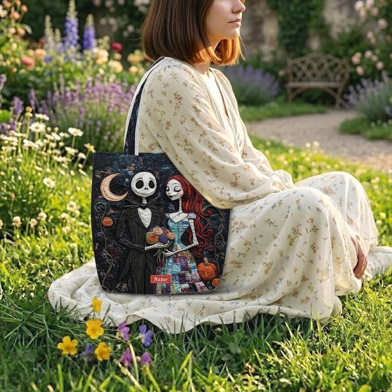 May include: A black tote bag featuring a printed illustration of Jack Skellington and Sally from The Nightmare Before Christmas. The design includes a crescent moon, a pumpkin, and a small red rectangular label with the word Name printed.