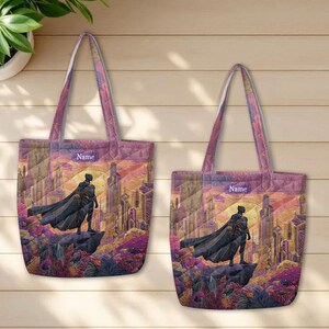 May include: Two quilted tote bags featuring a graphic illustration of a black superhero in a cape standing on a rock overlooking a futuristic city. The design includes a purple and orange sunset sky and a rectangular label with the text Name.