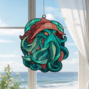 May include: Stained glass window hanging featuring a stylized depiction of a sea creature with tentacles, wearing a hat. The design incorporates shades of teal, green, and red. The word "Name" is printed on the hat. It hangs from a chain.