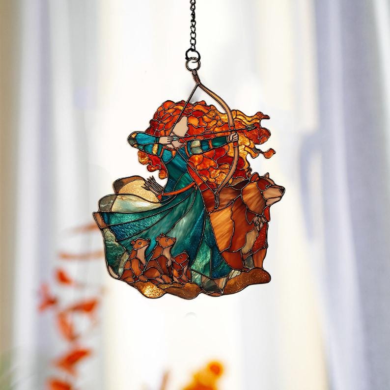 May include: Stained glass suncatcher featuring a red-haired archer in a teal and blue dress, drawing a bow. A brown bear and three smaller bear cubs are also depicted. The suncatcher hangs from a chain.