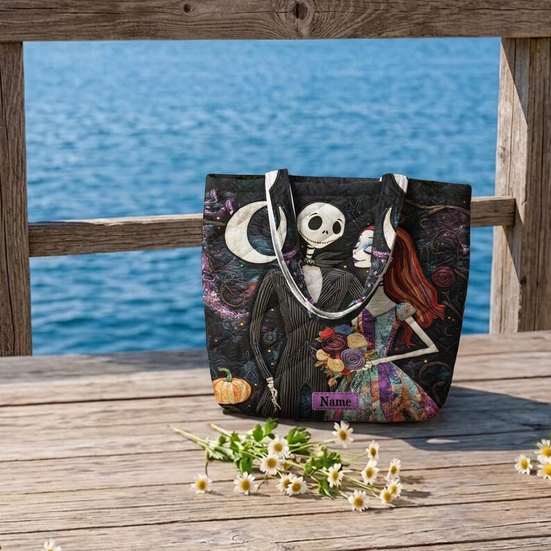May include: A black quilted tote bag featuring a graphic print of a skeleton character in a pinstripe suit and a female character with long red hair holding a bouquet. The bag includes a rectangular purple label with the text Name printed on it.