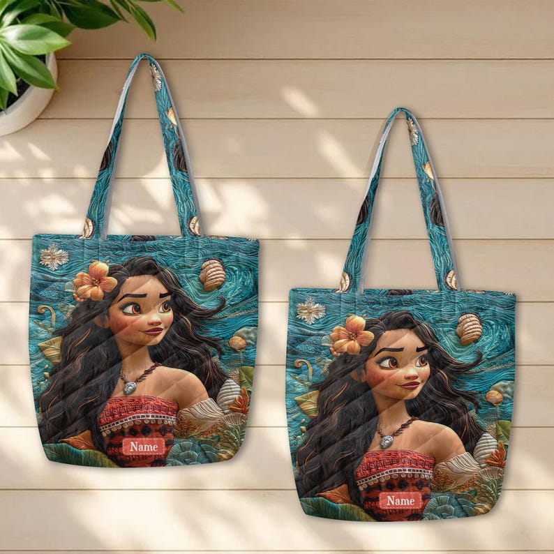 May include: Two tote bags featuring a printed illustration of a character with long dark hair, a yellow flower, and a patterned top against a blue ocean background. Each bag includes a rectangular label with the word Name printed in white text.