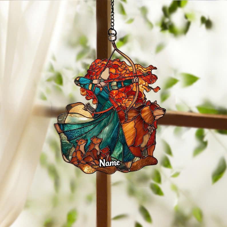 May include: Stained glass suncatcher featuring a woman with red hair aiming a bow and arrow, with a bear and three cubs. The woman wears a teal and blue dress. The word "Name" is written on the bottom.