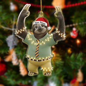 May include: A Christmas ornament featuring a cartoon sloth wearing a Santa hat with the text "Your Name". The sloth is dressed in a green shirt, yellow pants, and a striped tie, and is decorated with string lights.