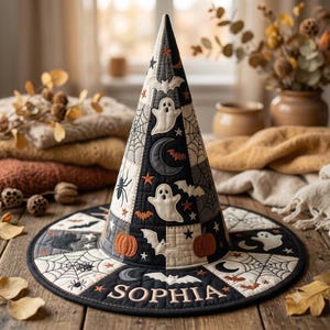 Op de afbeelding: Een doorgestikte heksenhoed met een patchworkontwerp in zwart, wit en oranje, voorzien van motieven van spoken, vleermuizen, spinnen, pompoenen, manen en spinnenwebben. De naam SOPHIA is in een schreeflettertype op de rand geborduurd.