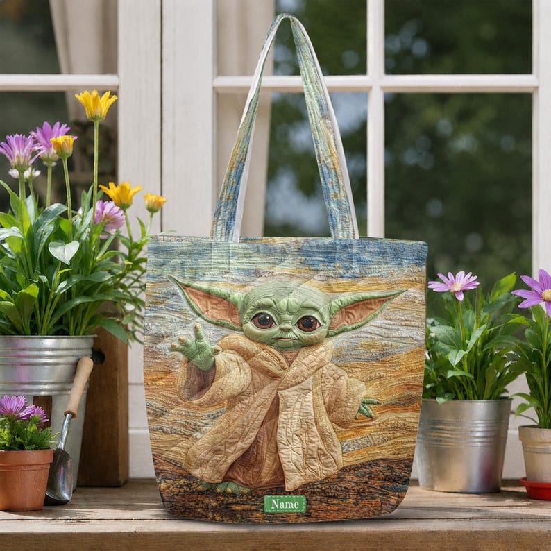 Puede incluir: Un bolso tote con un estampado estilo acolchado de una criatura verde de orejas grandes con una t&uacute;nica color canela. El fondo muestra un paisaje texturizado y pict&oacute;rico en tonos azules, amarillos y marrones. Una etiqueta verde dice Name.