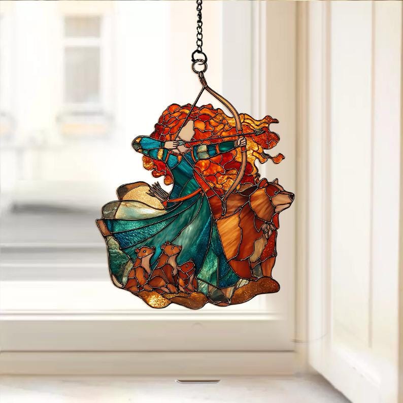 May include: Stained glass window hanging featuring a woman with red hair aiming a bow and arrow. The design includes a bear and three cubs, with a color palette of teal, orange, and brown. The artwork is suspended by a metal chain.