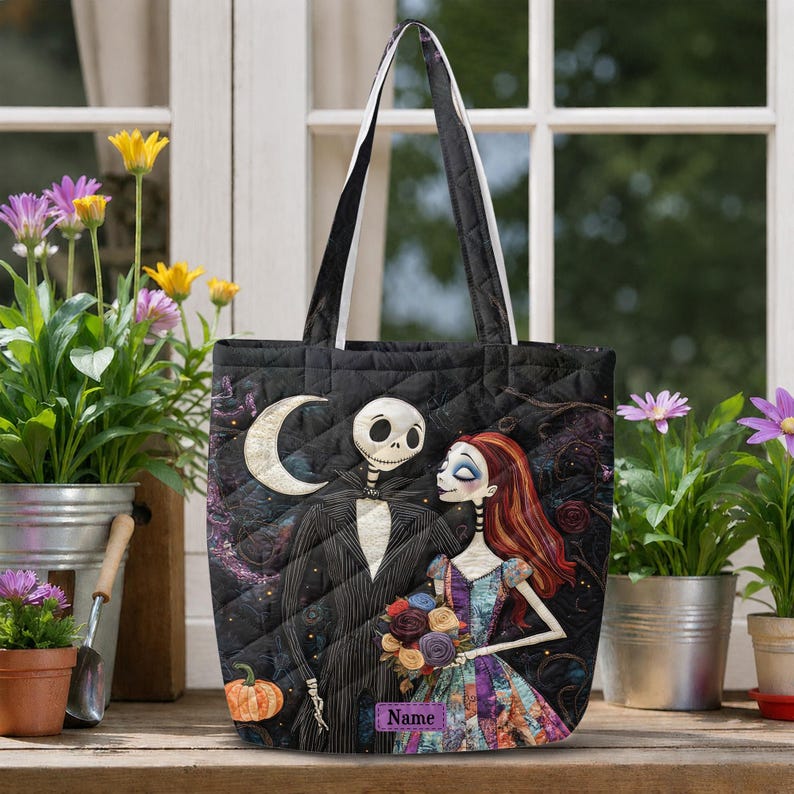 May include: A black quilted tote bag featuring a graphic print of a skeleton character in a pinstripe suit and a female character with long red hair holding a bouquet of flowers, with a crescent moon and a purple name tag labeled Name.
