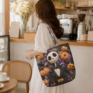 May include: A fabric tote bag featuring a printed graphic of a skeletal character in a pinstripe suit surrounded by orange jack-o'-lanterns against a dark purple and black swirling background. A small rectangular label with the text Name is visible.