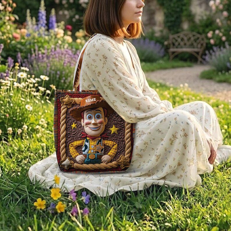 May include: A rectangular tote bag featuring a quilted brown background with a rope-style border and a central graphic of a cowboy character wearing a hat with the text NAME, a yellow plaid shirt, and a sheriff badge, with two white shoulder straps.