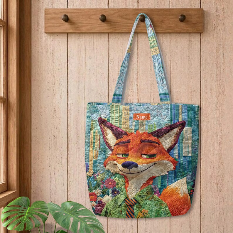 May include: A quilted tote bag featuring a graphic of a fox character with orange fur, green eyes, and a green shirt. The background displays a city skyline and flowers. A small rectangular patch with the text Name is centered above the fox.