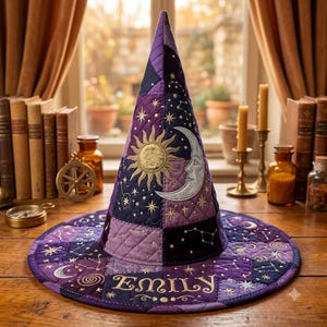 May include: A quilted pointed hat in shades of purple and dark blue, featuring embroidered gold sun and silver moon motifs, celestial star patterns, and the name Emily stitched in gold thread along the wide, circular brim of the hat.