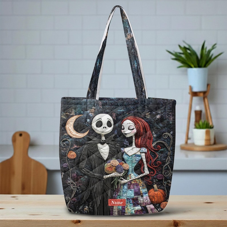 May include: A quilted tote bag featuring a dark, patterned design with a skeletal figure in a pinstripe suit and a female figure with long red hair holding a bouquet of flowers. A crescent moon and a pumpkin are visible, with the word Name printed.