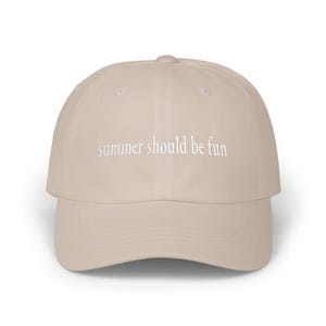 May include: A beige baseball cap with a curved brim. The cap features the embroidered text "summer should be fun" in white. The hat is a neutral color, suitable for various outfits and occasions.