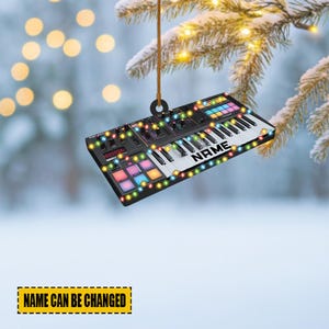 May include: A black and white keyboard ornament with colorful lights and the word "NAME" on the keys. The ornament is hanging from a brown string. The text "NAME CAN BE CHANGED" is at the bottom.