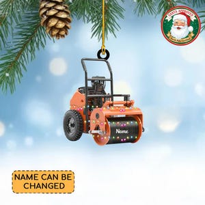 May include: Orange and black construction roller ornament with a string of lights. The ornament has a black roller with the word "Name" on it. The ornament is hanging from a gold string. The text "Name can be changed" is on a yellow rectangle.