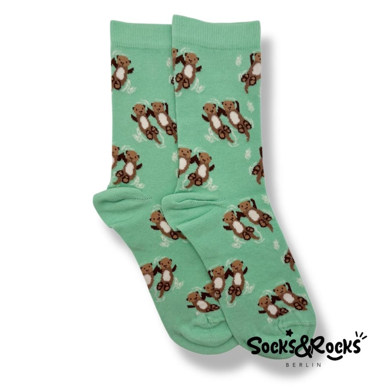 May include: A pair of mint green socks featuring a repeating pattern of brown otters swimming in water. The socks have a ribbed cuff and the brand name "Socks & Rocks" is printed in black on the side.