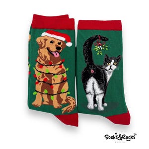 Può includere: Un paio di calze di Natale verdi con un golden retriever che indossa un cappello di Babbo Natale e luci natalizie e un gatto bianco e nero con il vischio sulla coda.