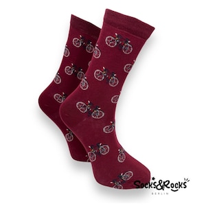 Könnte beinhalten: Ein Paar burgunderfarbene Socken mit einem weißen Fahrradmuster. Die Socken haben den Text "Socks & Rocks Berlin" auf der Unterseite.