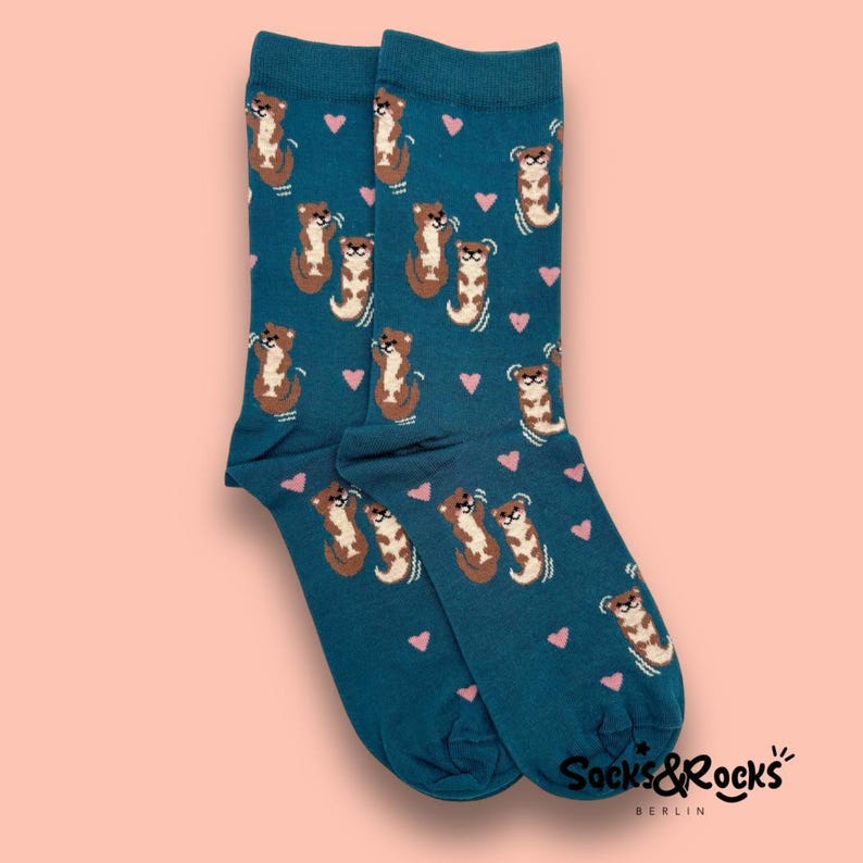 May include: Teal socks with a repeating pattern of brown otters and pink hearts. The socks have the text "Socks & Rocks Berlin" printed on the bottom.