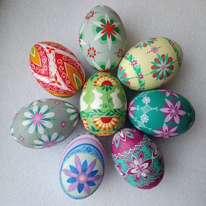 Puede incluir: Ocho huevos de Pascua pintados a mano con varios diseños coloridos. Los huevos están decorados con flores, patrones geométricos y animales.