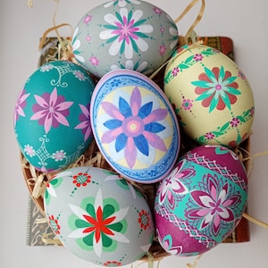 Puede incluir: Seis huevos de Pascua pintados a mano con diferentes diseños florales. Los huevos están pintados en tonos de azul, verde, rosa, amarillo y blanco.