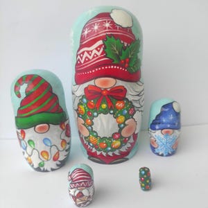 May include: A set of six hand-painted wooden nesting dolls, each depicting a gnome in festive holiday attire. The gnomes wear red and green hats, some with lights and snowflakes. The largest gnome holds a wreath.