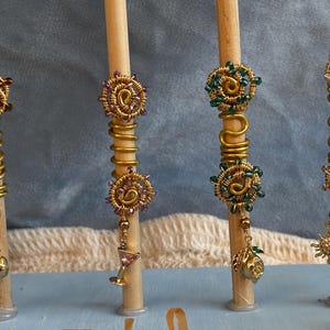 May include: Four gold-toned wire hair coils wrapped around wooden dowels. Each coil features intricate wire-wrapped spirals adorned with small beads in brown, purple, green, and clear. Dangling charms include a pomegranate, martini glass, lemon, and sun.