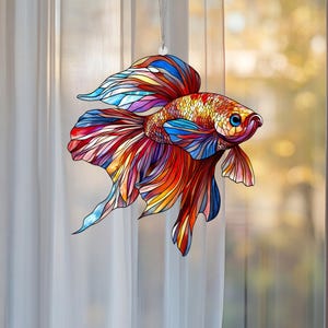 May include: A stained glass window hanging depicting a colourful betta fish with red, orange, yellow, blue and purple scales. The fish is in a swimming position with its fins spread out.