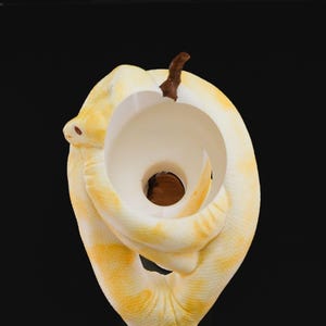 Może przedstawiać: Biała ceramiczna rzeźba węża z ż&oacute;łtym i pomarańczowym wzorem. Wąż jest zwinięty w k&oacute;łko, z ogonem w pysku. Rzeźba jest unikalnym i dekoracyjnym elementem do każdego domu.