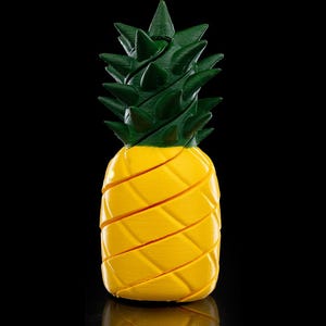 Könnte beinhalten: Eine gelbe und grüne 3D-gedruckte Ananas mit einer strukturierten Oberfläche. Die Ananas befindet sich auf einem schwarzen Hintergrund.