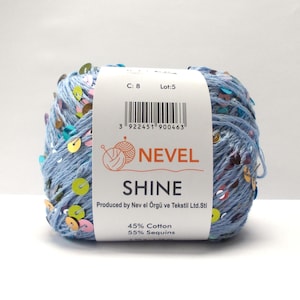 Op de afbeelding: Bol lichtblauw garen met kleurrijke pailletten. Het etiket luidt "NEVEL SHINE" en geeft aan dat het garen 45% katoen en 55% pailletten bevat. Het etiket bevat ook een barcode en de tekst "Produced by Nev el Örgü ve Tekstil Ltd.Sti."