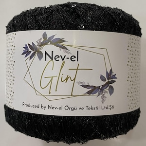 Puede incluir: Un carrete de hilo negro con una etiqueta que dice "Nev-el Glint". El hilo parece tener una textura brillante y con lentejuelas. La etiqueta presenta un diseño geométrico con detalles florales y el texto "Produced by Nev-el Örgü ve Tekstil Ltd.Şti."