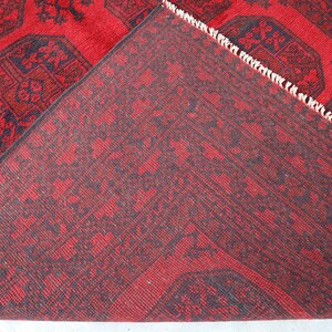 Puede incluir: Una alfombra roja y azul marino con un dise&ntilde;o detallado. La alfombra est&aacute; doblada, revelando la parte inferior con un patr&oacute;n similar. Los bordes tienen flecos blancos.