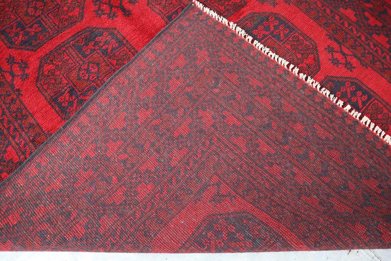 Puede incluir: Una alfombra roja y azul marino con un dise&ntilde;o detallado. La alfombra est&aacute; doblada, revelando la parte inferior con un patr&oacute;n similar. Los bordes tienen flecos blancos.