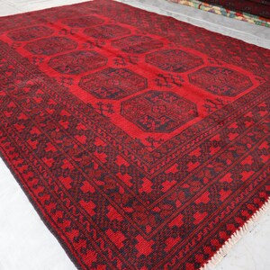 Puede incluir: Una alfombra rectangular roja con un patr&oacute;n oscuro. La alfombra presenta un dise&ntilde;o central de formas geom&eacute;tricas y un borde detallado. La alfombra est&aacute; hecha de material tejido y es adecuada para la decoraci&oacute;n del hogar.