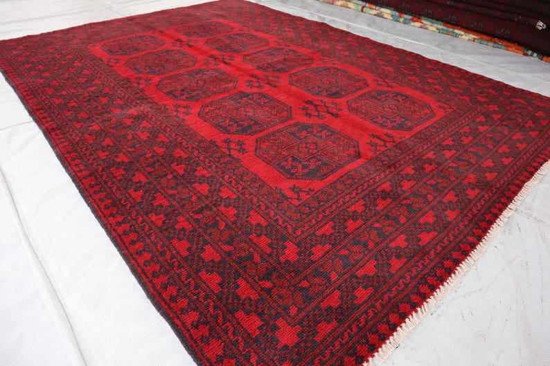 Puede incluir: Una alfombra rectangular roja con un patr&oacute;n oscuro. La alfombra presenta un dise&ntilde;o central de formas geom&eacute;tricas y un borde detallado. La alfombra est&aacute; hecha de material tejido y es adecuada para la decoraci&oacute;n del hogar.