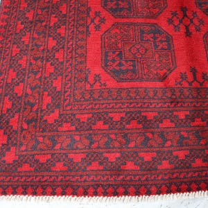 Puede incluir: Secci&oacute;n de una alfombra estampada en rojo y negro. La alfombra presenta dise&ntilde;os geom&eacute;tricos y un borde con un patr&oacute;n repetitivo. La combinaci&oacute;n de colores de la alfombra es principalmente roja con acentos negros y tiene un borde con flecos.