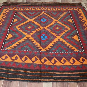 May include: A colorful rug with a geometric pattern in shades of orange, red, blue, and green. The rug has a traditional design with a central diamond shape surrounded by smaller geometric shapes.