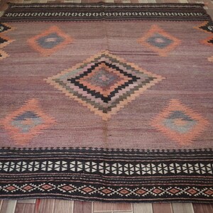 May include: A vintage rug with a geometric pattern in shades of pink, orange, black, and gray. The rug has a diamond-shaped design with a border of black and white.