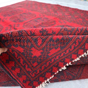 Puede incluir: Una alfombra roja doblada con un patr&oacute;n oscuro. La alfombra tiene un dise&ntilde;o geom&eacute;trico con un fondo rojo y acentos oscuros. El borde de la alfombra es visible, mostrando una franja.