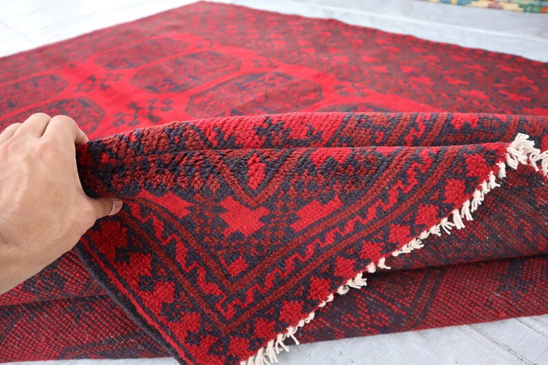 Puede incluir: Una alfombra roja doblada con un patr&oacute;n oscuro. La alfombra tiene un dise&ntilde;o geom&eacute;trico con un fondo rojo y acentos oscuros. El borde de la alfombra es visible, mostrando una franja.