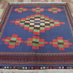 May include: A blue rug with a geometric pattern in shades of red, green, and brown. The rug has a fringe border.