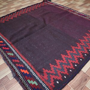 May include: A dark brown rug with a geometric pattern in shades of red, blue, green, and white. The rug has a fringe border.