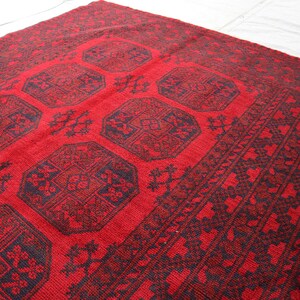 Puede incluir: Una alfombra roja y negra con dise&ntilde;os geom&eacute;tricos. La alfombra presenta un campo central rojo con motivos octogonales negros repetidos, rodeado por un borde detallado. La alfombra est&aacute; hecha de material tejido.