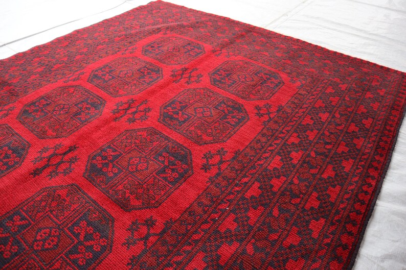 Puede incluir: Una alfombra roja y negra con dise&ntilde;os geom&eacute;tricos. La alfombra presenta un campo central rojo con motivos octogonales negros repetidos, rodeado por un borde detallado. La alfombra est&aacute; hecha de material tejido.