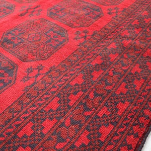 Puede incluir: Primer plano de una alfombra roja con un patr&oacute;n geom&eacute;trico. La alfombra presenta un dise&ntilde;o repetitivo de formas octogonales en rojo m&aacute;s oscuro y azul marino. El borde tiene un patr&oacute;n floral repetitivo.