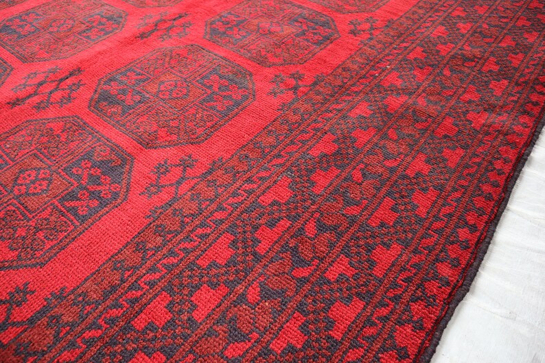 Puede incluir: Primer plano de una alfombra roja con un patr&oacute;n geom&eacute;trico. La alfombra presenta un dise&ntilde;o repetitivo de formas octogonales en rojo m&aacute;s oscuro y azul marino. El borde tiene un patr&oacute;n floral repetitivo.
