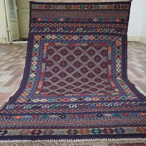 May include: A traditional rug with a dark blue background and intricate geometric patterns in shades of red, white, and beige. The rug has a fringe border.