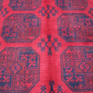 Puede incluir: Primer plano de una alfombra roja con un patr&oacute;n geom&eacute;trico repetitivo. El dise&ntilde;o presenta formas octogonales en tonos de rojo y azul oscuro, con detalles intrincados. La alfombra tiene una superficie texturizada.